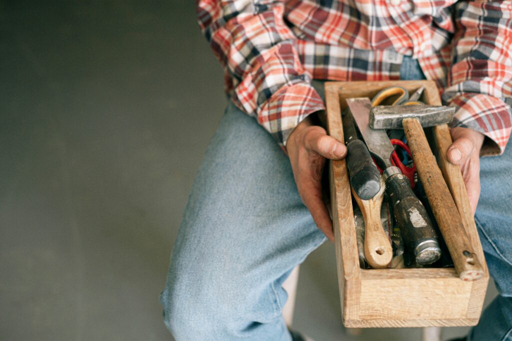A woodworker holding a toolbox filled with essential tools like hammers and screwdrivers.